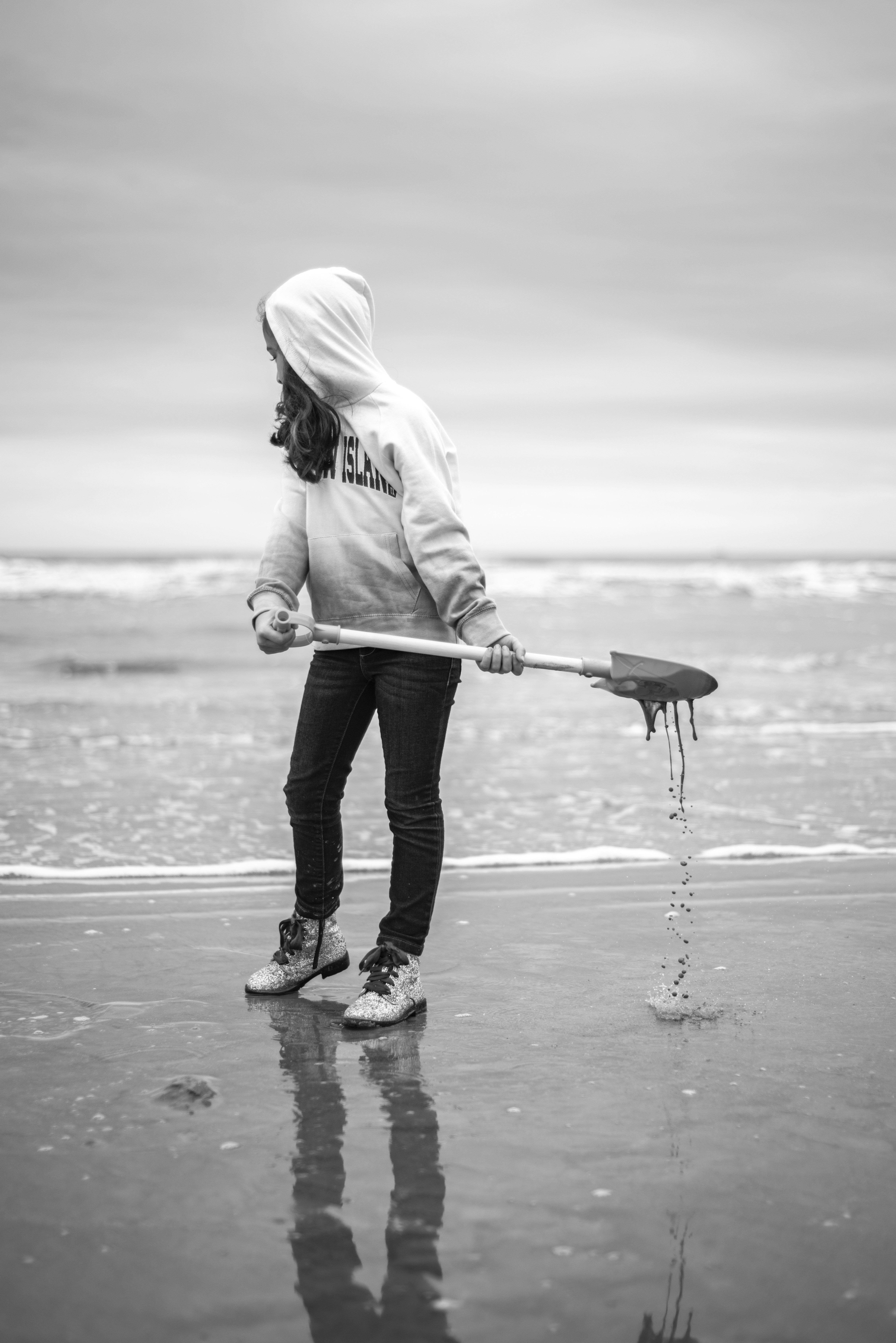 Woman in white hoodie holding umbrella walking on beach