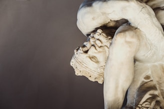 A marble statue depicting a muscular figure in a dynamic, twisting pose. The detailed facial expression and robust physique suggest classical influences. The texture of the stone is smooth and polished, showcasing expert craftsmanship.