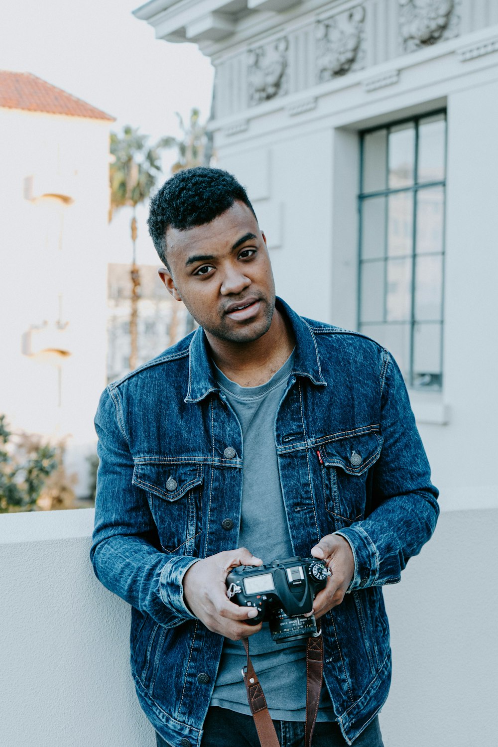 man in blue denim jacket holding black camera