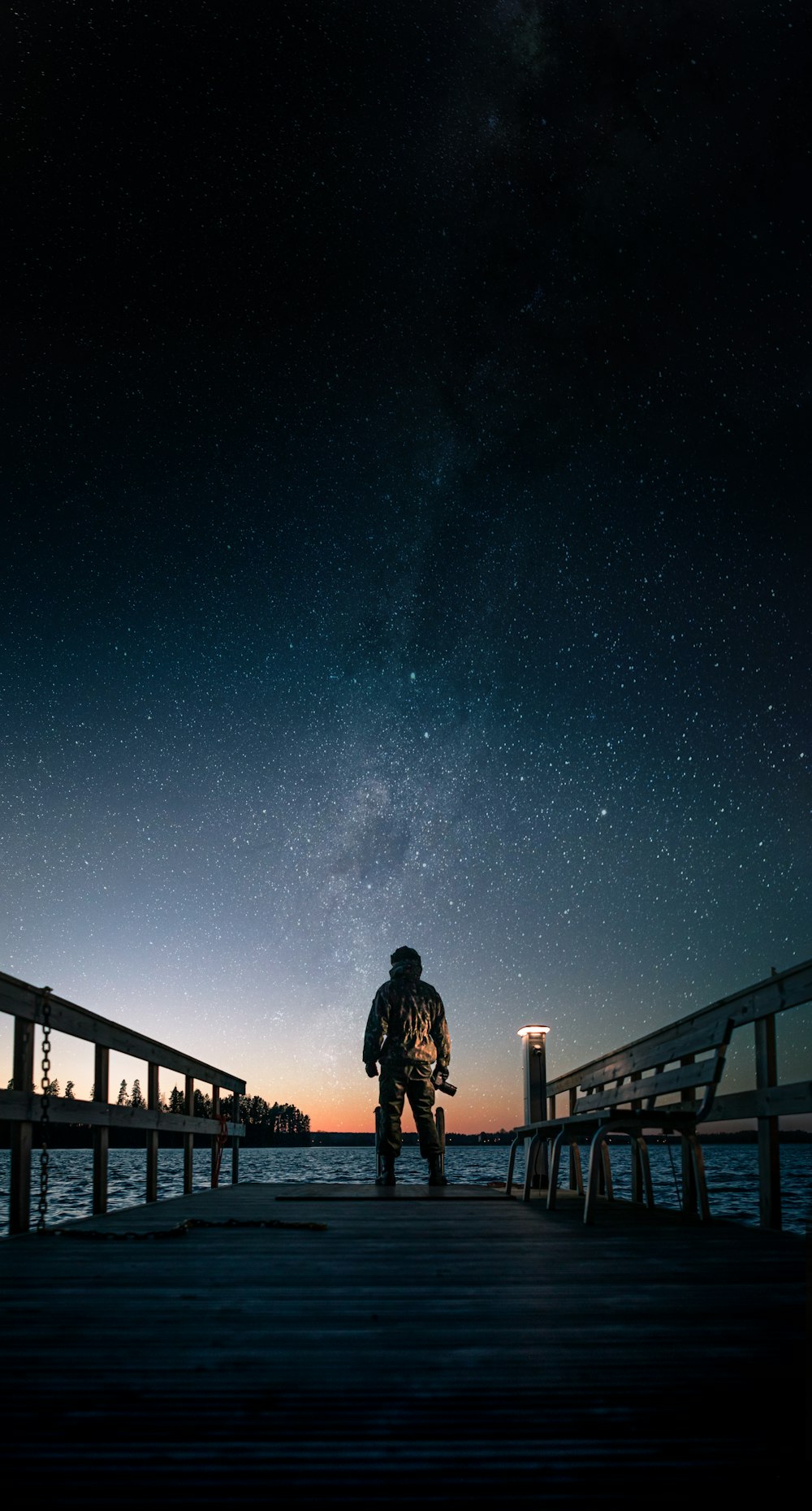 uomo in giacca nera in piedi sul ponte di legno marrone sotto la notte stellata