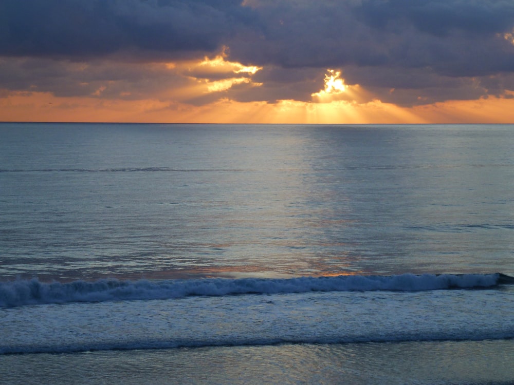 ocean waves under cloudy sky during sunset