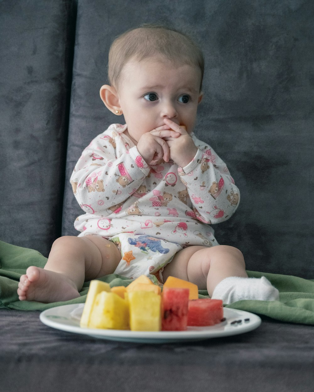 baby in white and pink onesie sitting on green and white ceramic plate