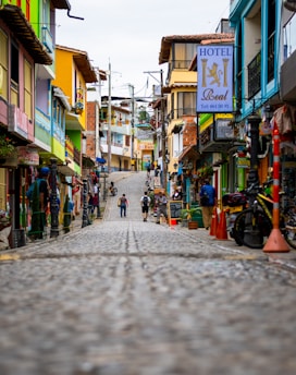A vibrant street scene in a historic town with colorful storefronts and people walking.