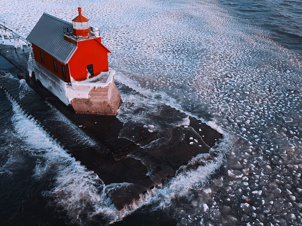 Maison blanche et rouge sur une formation rocheuse noire à côté d’un plan d’eau pendant la journée