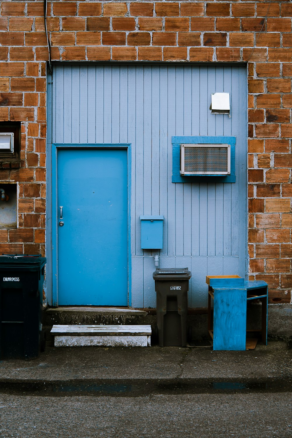 blue and black trash bin beside blue wooden door