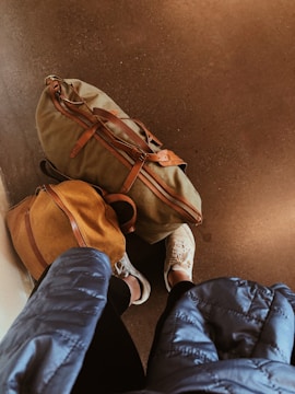 person in blue denim jeans and white sneakers standing beside brown backpack