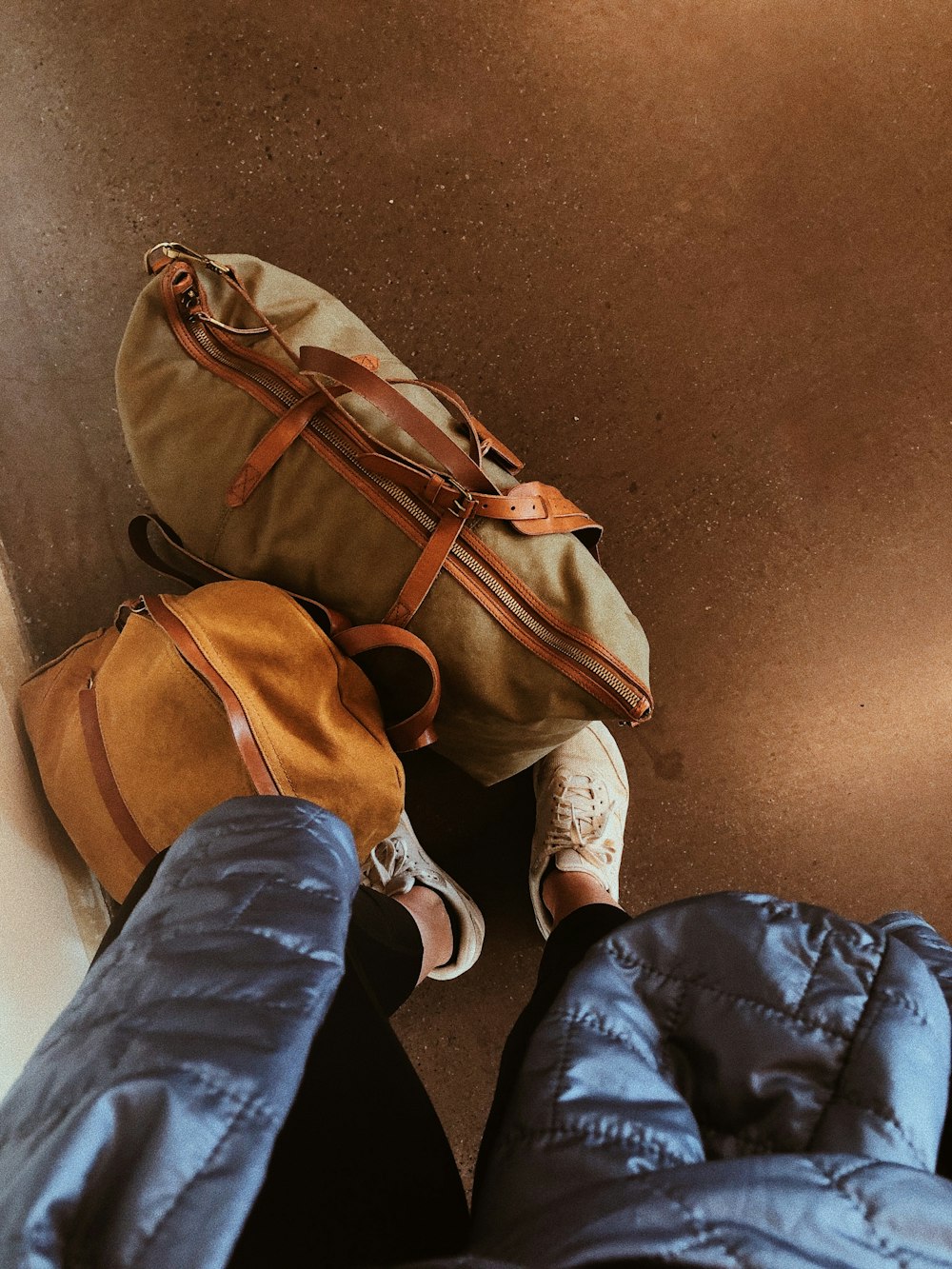 person in blue denim jeans and white sneakers standing beside brown backpack