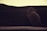 A small rodent, possibly a rat or mouse, appears to be climbing or looking up towards a stack of dark fabrics against a softly lit background.
