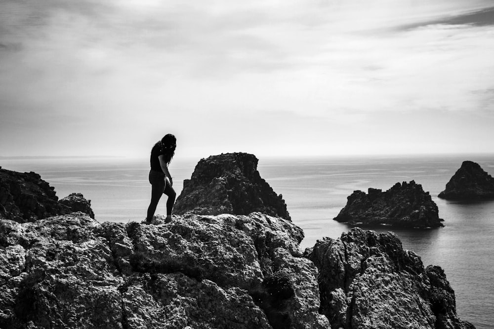 silhouette of woman standing on rock formation near body of water during daytime