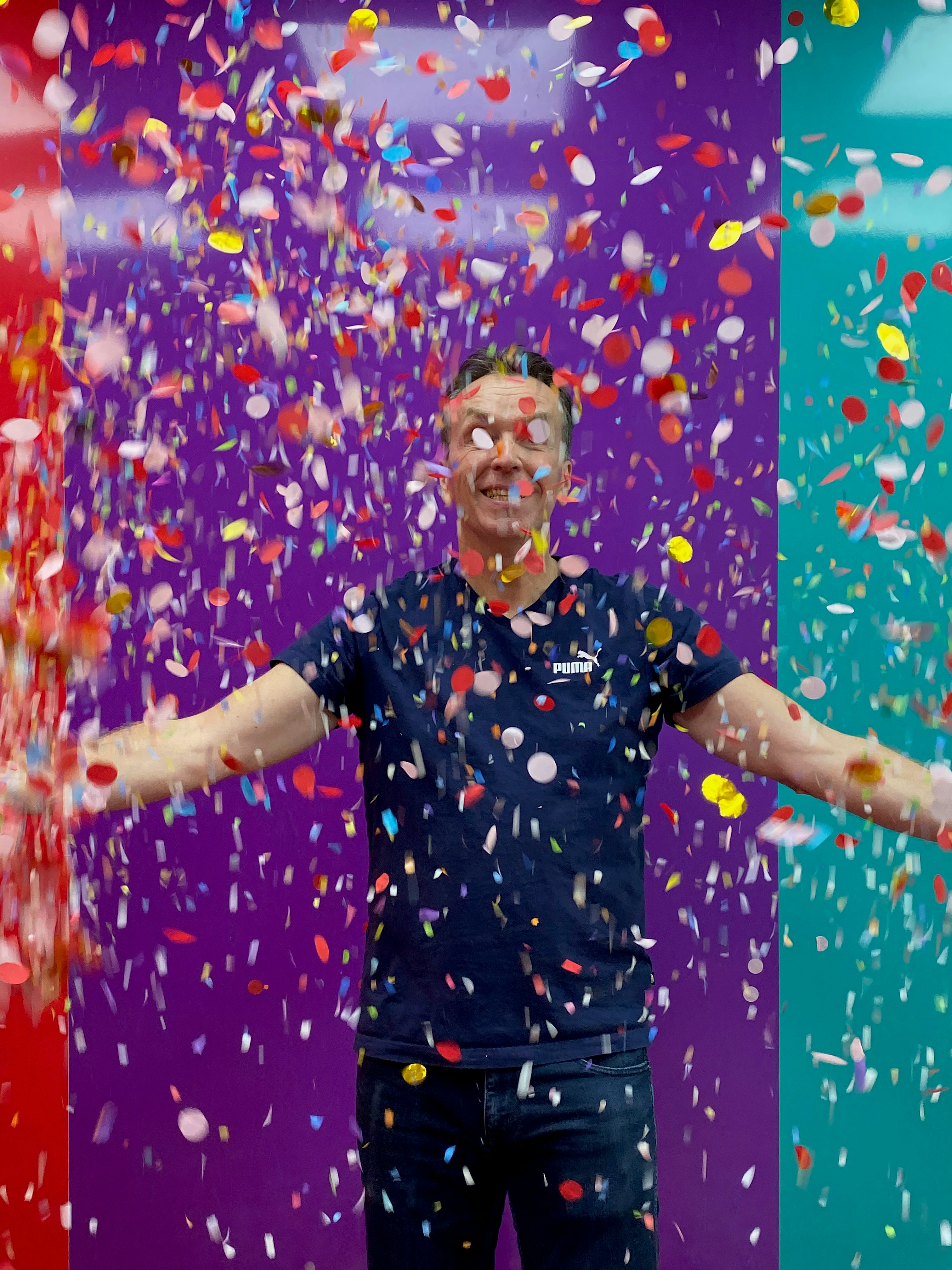 Hombre con camiseta azul celebrando con confeti cayendo.