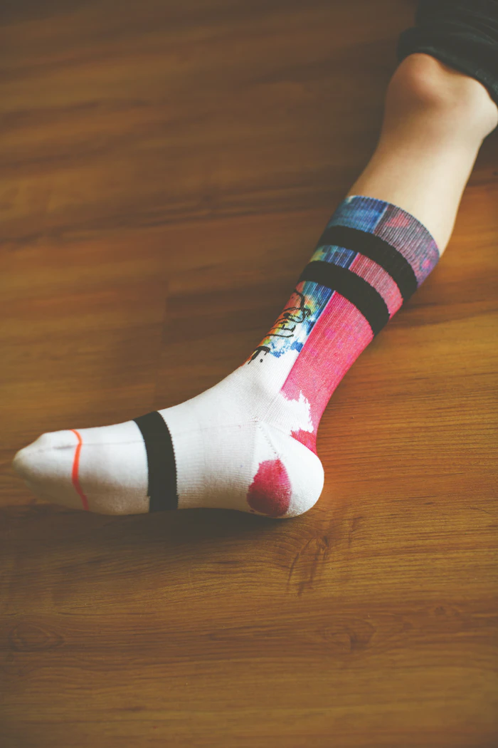 White sport sock with a vivid graphic print resting on a wooden floor