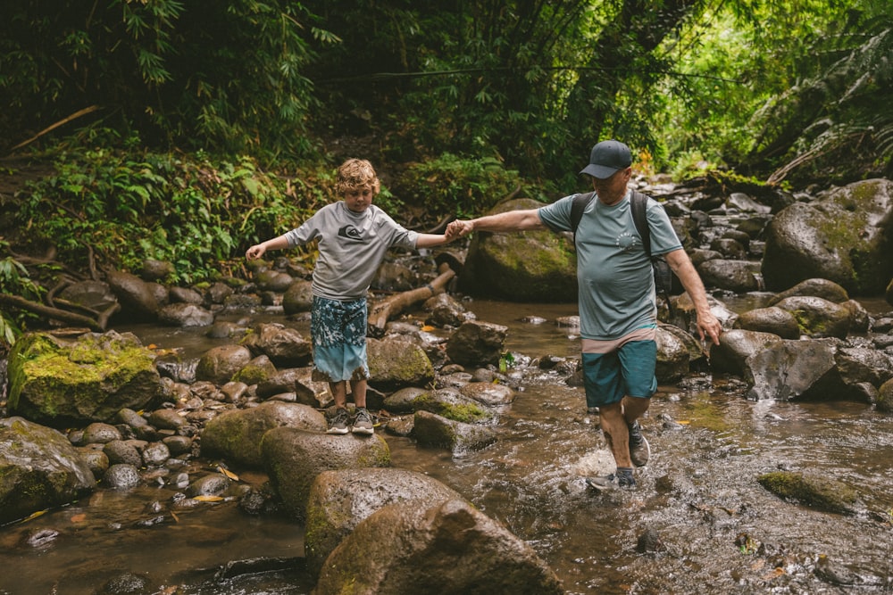 man in grey t-shirt and blue denim shorts standing on rocky river during daytime