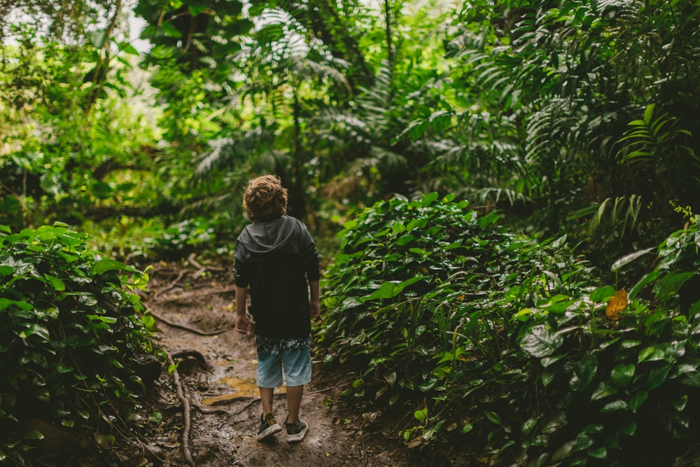 man in black t-shirt walking on dirt pathway between green plants during daytime