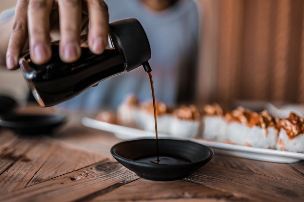 personne versant du café sur une tasse en céramique noire