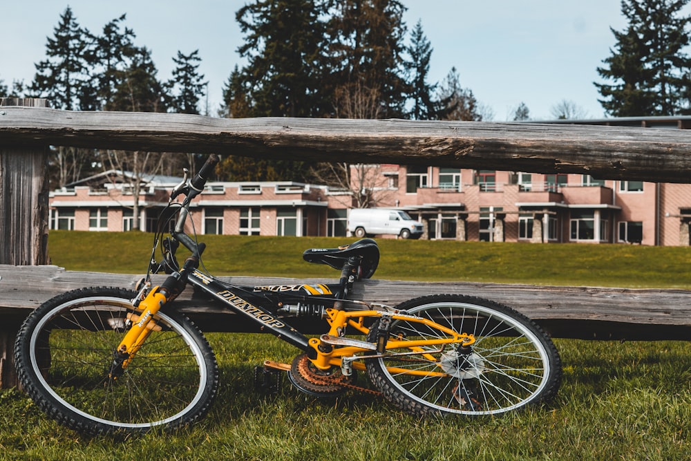 Bicicleta de montaña rígida negra y amarilla estacionada junto a una valla de madera marrón durante el día