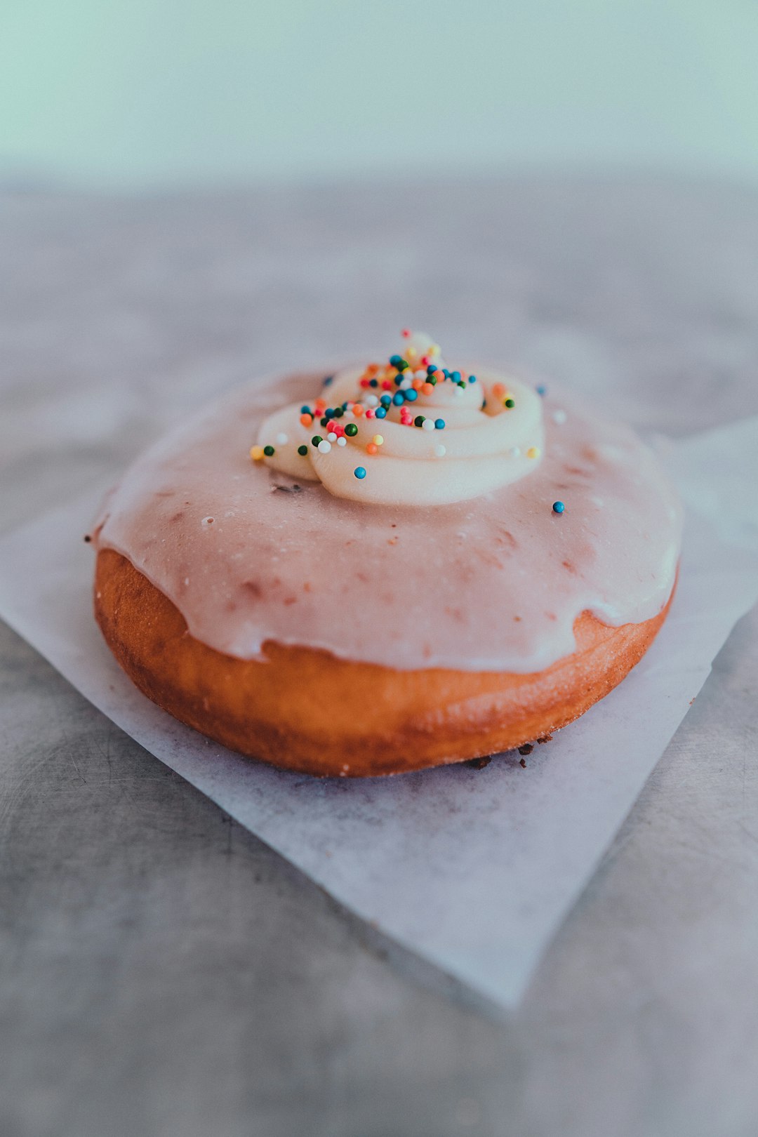 brown doughnut with white icing and sprinkles on white paper