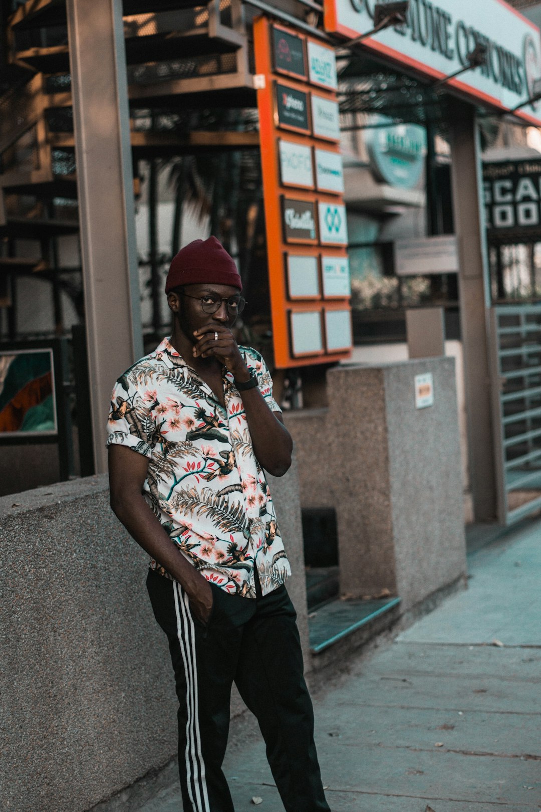 man in white red and black floral t-shirt and black pants standing on sidewalk during