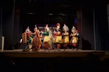 A colorful troupe performing traditional dance in elaborate costumes under bright stage lights.