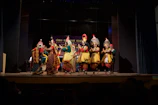 Children in vibrant traditional Canarian carnival costumes performing on stage with red and gold decorations.