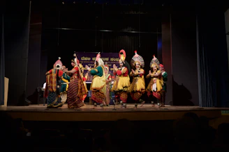 Children in colorful traditional Canarian carnival costumes performing on stage with vibrant red and black decorations.