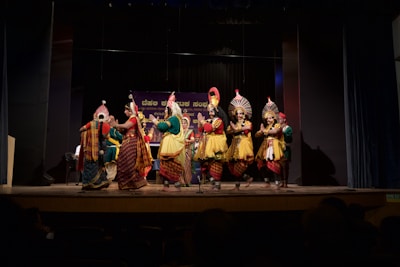 A colorful troupe performing traditional dance in elaborate costumes under bright stage lights.