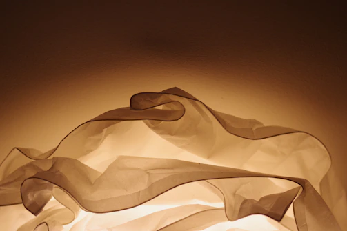 An artistic installation featuring layered translucent fabrics illuminated with soft light.