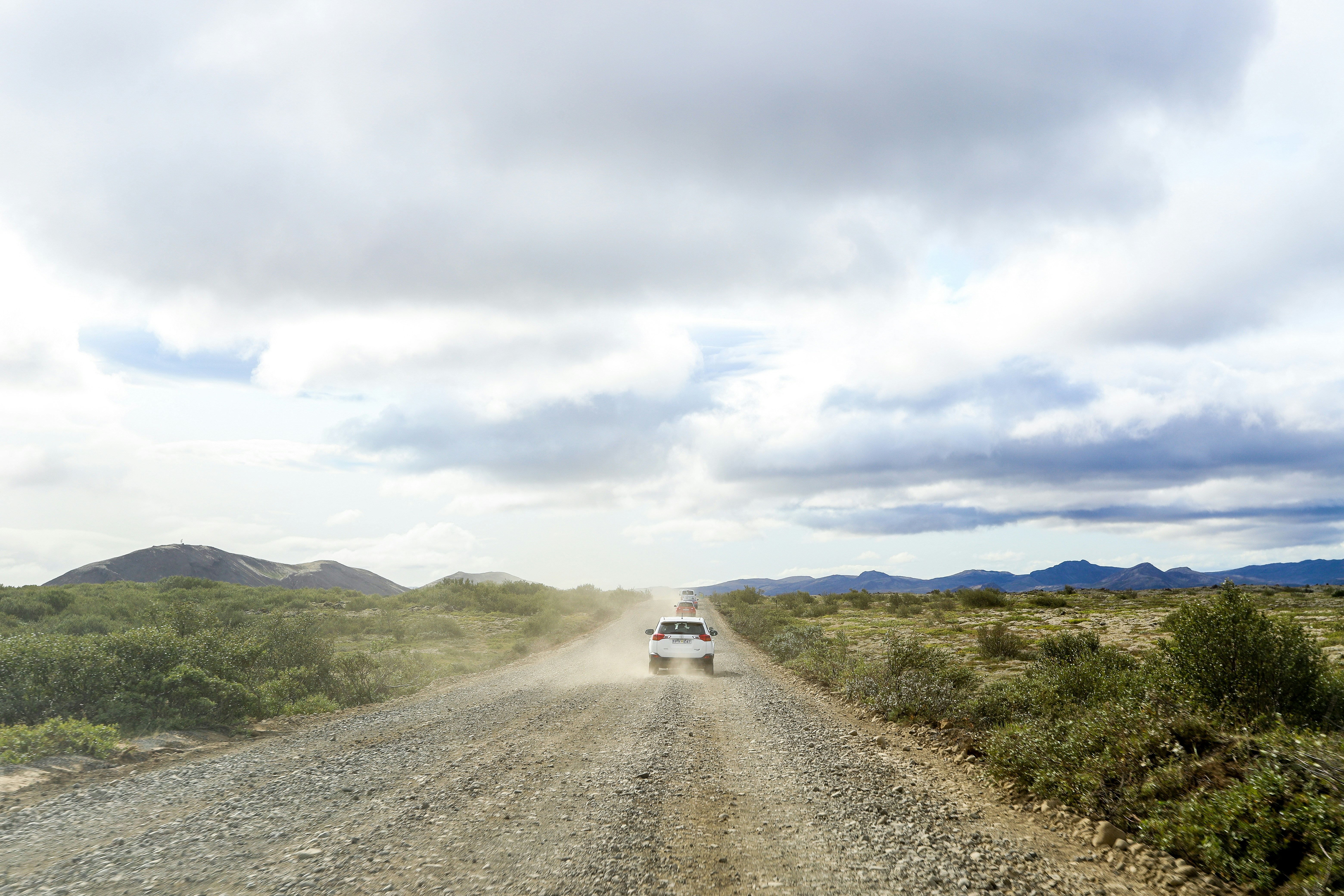 white car on road between green grass field under white clouds during daytime gravel teams background