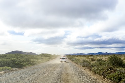 white car on road between green grass field under white clouds during daytime gravel zoom background