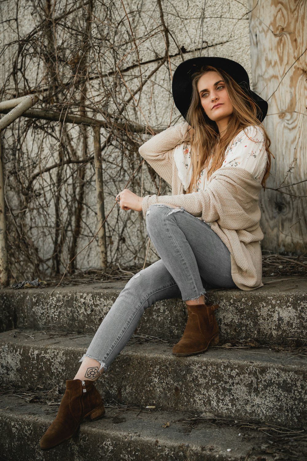 woman in white sweater and blue denim jeans sitting on concrete pavement