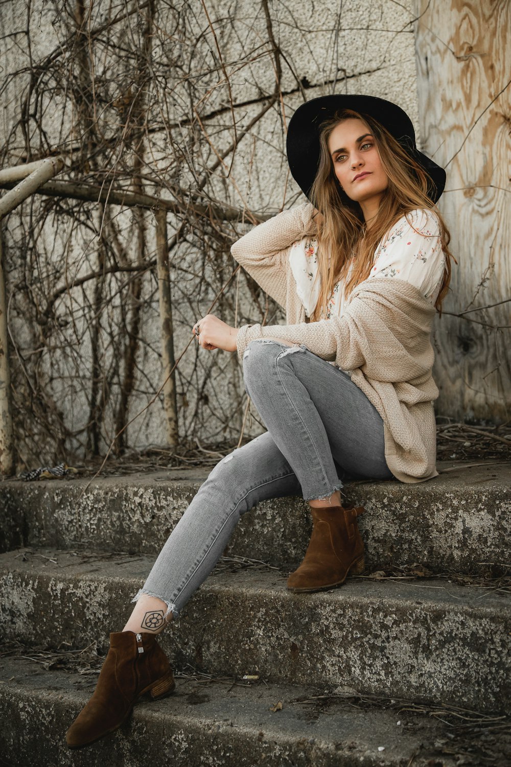 Mujer en suéter blanco y jeans de mezclilla azul sentada en pavimento de concreto