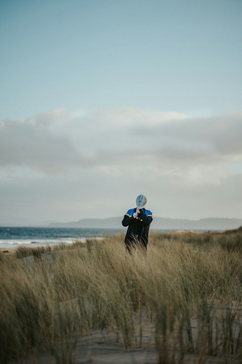 person in black jacket standing on brown grass field near body of water during daytime