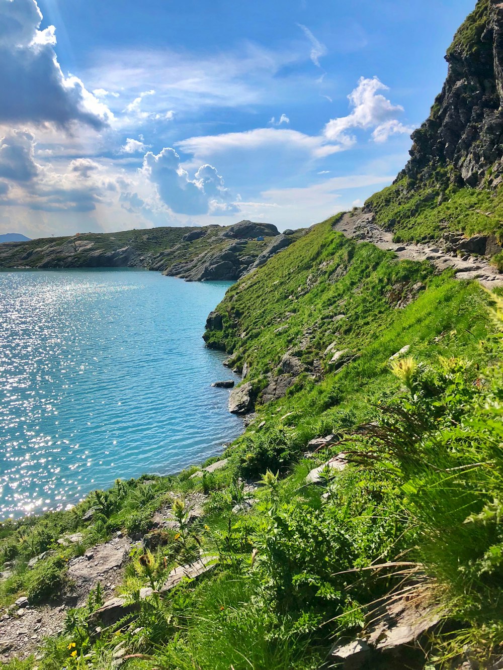 昼間の青と白の曇り空の下に青い海のそばの緑と茶色の山