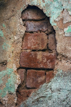A weathered and peeling plaster wall reveals aged, reddish-brown bricks beneath. The worn surface has patches of green paint and crumbling texture, giving a rustic and abandoned feel.