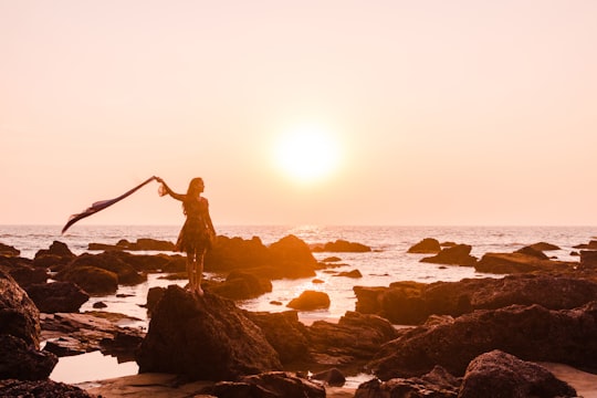 woman in black tank top standing on rock formation near sea during daytime in Arambol India