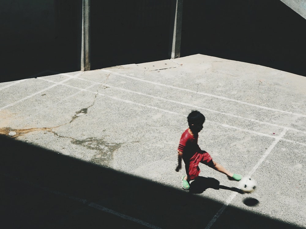boy in red and white long sleeve shirt playing soccer during daytime