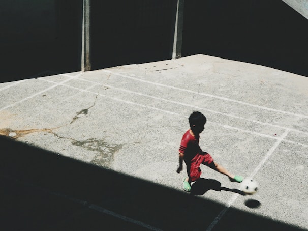 boy in red and white long sleeve shirt playing soccer during daytime
