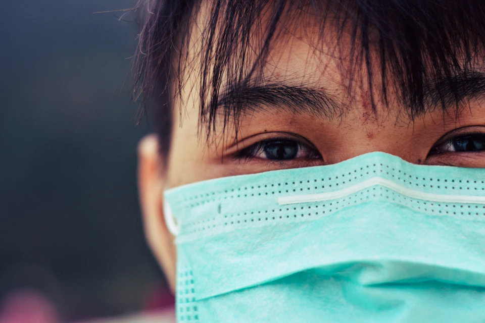 Person's face partially obscured by light blue surgical mask covering eyes and nose