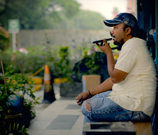 man in white t-shirt and blue denim jeans sitting on concrete bench using black dslr in Cikarang Indonesia