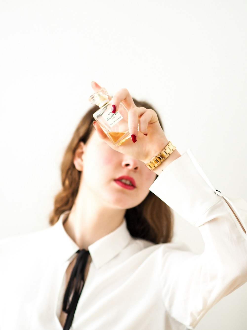 woman in white dress shirt holding clear glass bottle