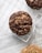 A close-up view of two chocolate cookies with chunks placed on a cooling rack over a newspaper. The cookies have a rustic, homemade appearance with visible chocolate pieces and a textured surface
