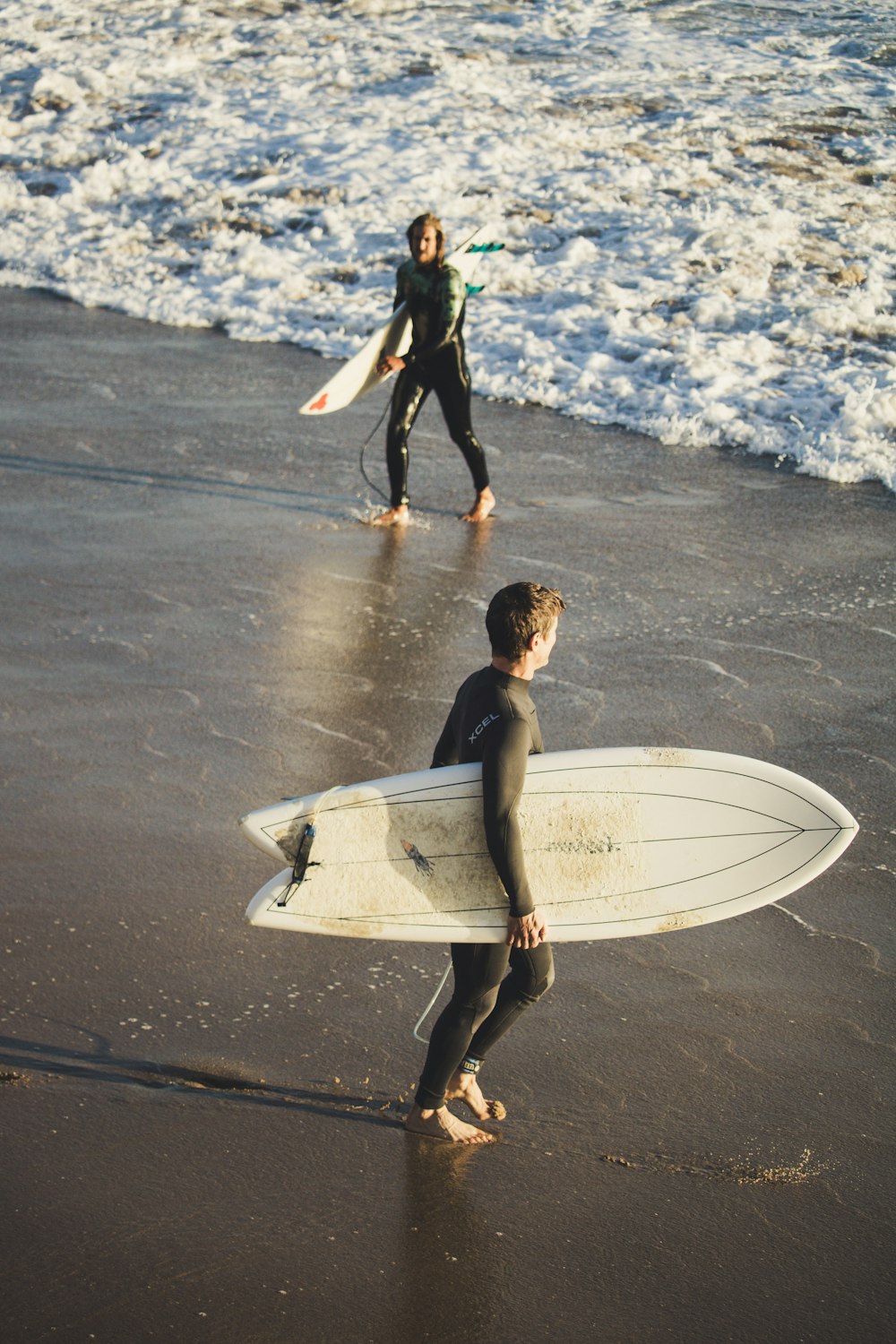 man in black suit holding white surfboard walking on wet road during daytime