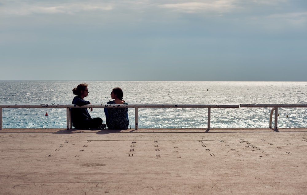 2 person sitting on bench near sea during daytime