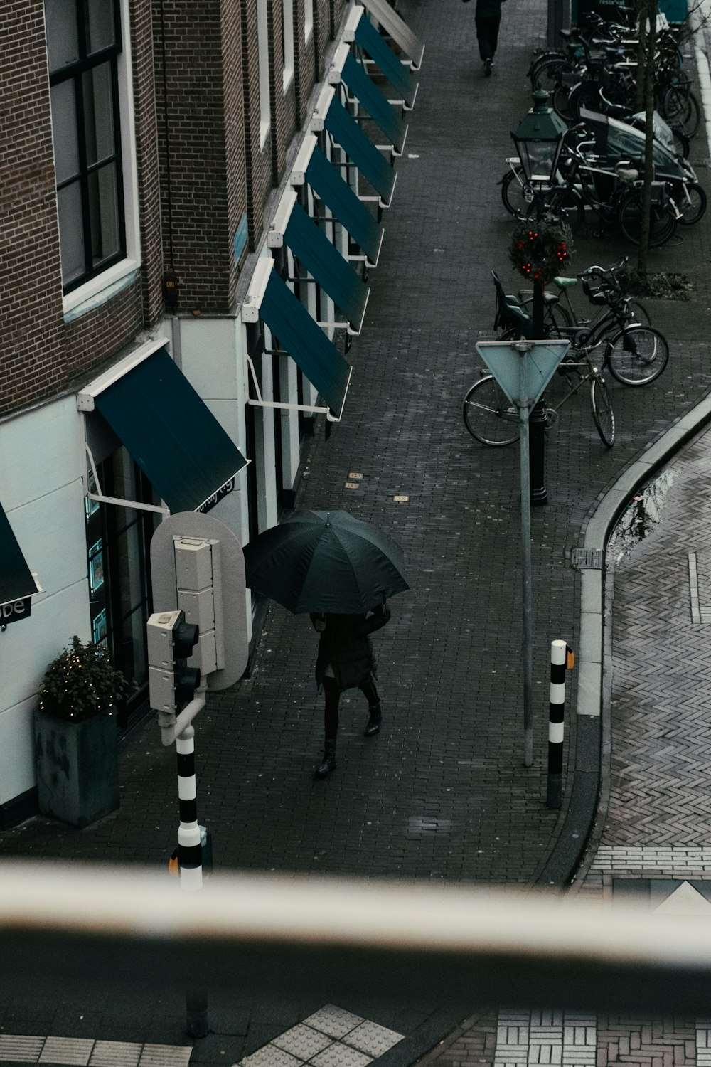 persona con chaqueta negra sosteniendo paraguas caminando por la acera durante el día