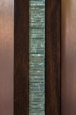 A vertical stack of translucent blue-green glass panes is set within a dark brown wooden frame. The glass has a slightly wavy texture, creating an interesting visual pattern, while the wood provides a contrasting background, highlighting the glass feature.