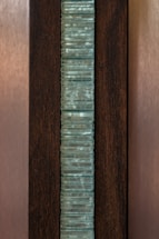 A vertical stack of translucent blue-green glass panes is set within a dark brown wooden frame. The glass has a slightly wavy texture, creating an interesting visual pattern, while the wood provides a contrasting background, highlighting the glass feature.