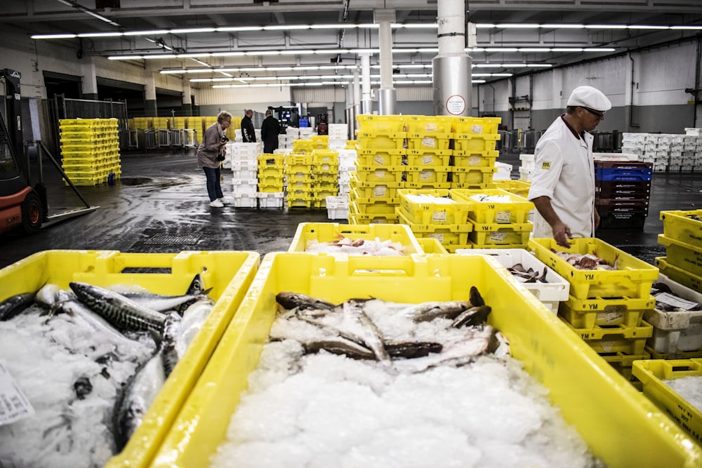 man in white shirt and black pants standing beside yellow plastic crates