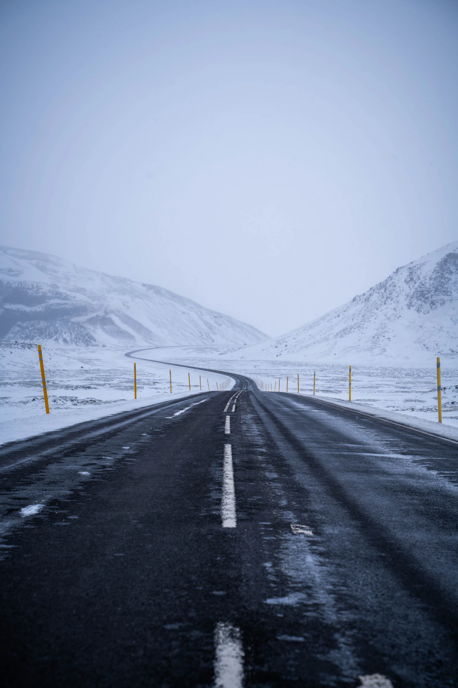 A road below snow-covered mountains in changing visibility