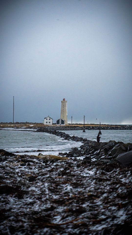 white lighthouse on rocky shore during daytime in Grótta Iceland