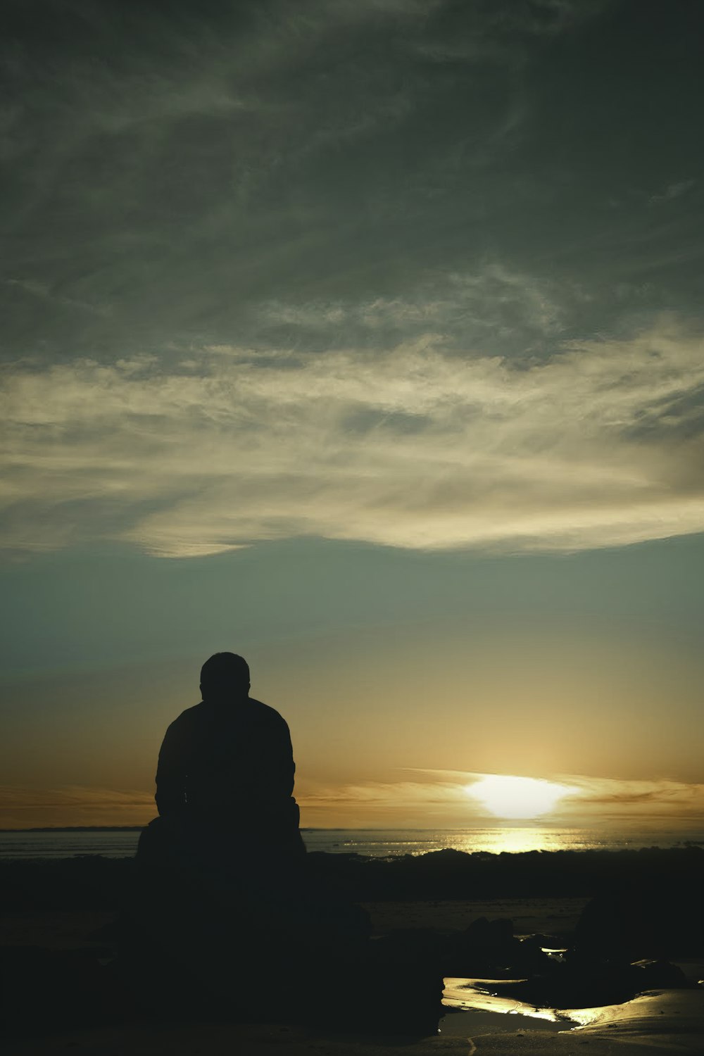 silhouette of man standing on seashore during sunset