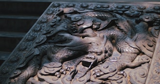 A detailed stone carving of a dragon with intricate patterns and flowing lines. The carving is skillfully executed, showing the dragon's scales, claws, and fierce expression, set against an ornate background that adds depth and complexity.